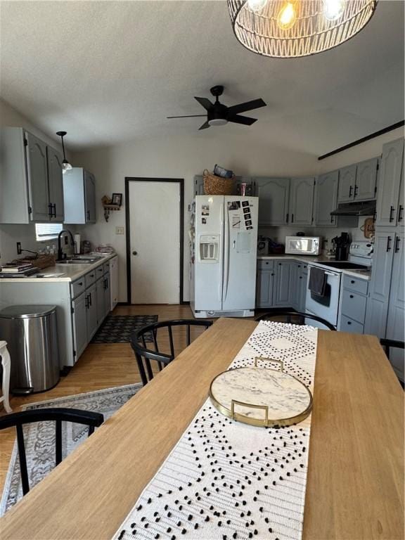 kitchen featuring white appliances, a sink, under cabinet range hood, and gray cabinetry