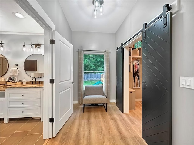hall featuring a barn door, a sink, light wood-type flooring, and baseboards