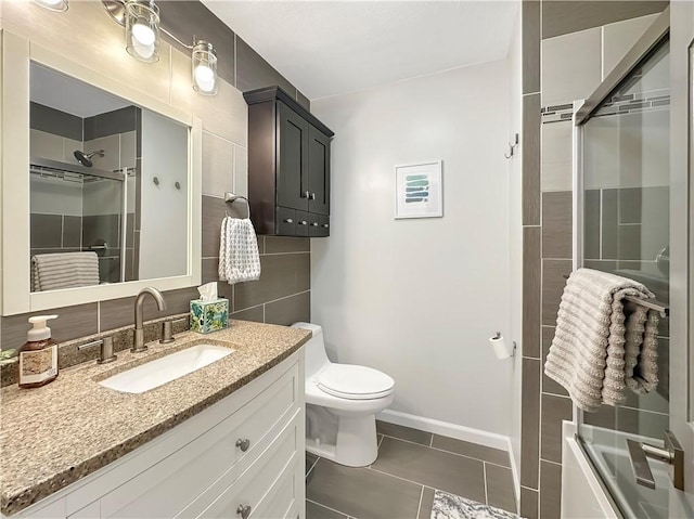 bathroom with a shower with shower door, toilet, vanity, tile walls, and tile patterned floors