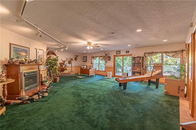 5353 E Reas Bridge Rd, Decatur, IL 62521 - recreation room with wallpapered walls, a textured ceiling, carpet flooring, ceiling fan, and a glass covered fireplace