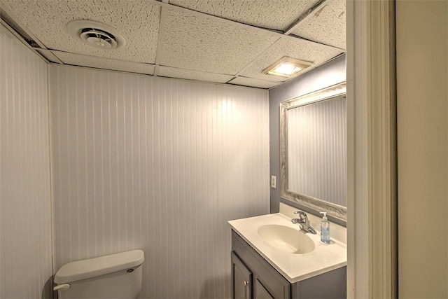 half bath with visible vents, vanity, toilet, and a drop ceiling