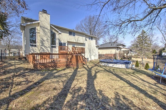 back of property with fence, a wooden deck, a fenced in pool, a trampoline, and a chimney