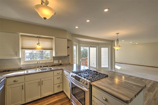 kitchen featuring tasteful backsplash, dark countertops, gas stove, a sink, and a peninsula