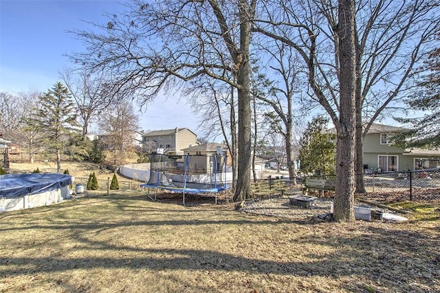 view of yard featuring an outdoor fire pit, a trampoline, fence, and a covered pool