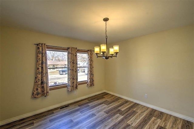 empty room featuring a chandelier, dark wood-style flooring, visible vents, and baseboards