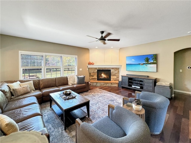 living area featuring arched walkways, a fireplace, dark wood-type flooring, ceiling fan, and baseboards