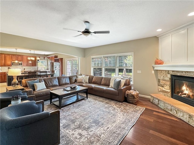 living room featuring a textured ceiling, arched walkways, a stone fireplace, hardwood / wood-style flooring, and a ceiling fan