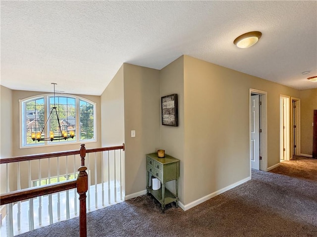 hallway featuring baseboards, an inviting chandelier, a textured ceiling, an upstairs landing, and carpet floors