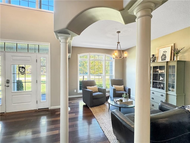 living room featuring arched walkways, a notable chandelier, baseboards, dark wood-style floors, and decorative columns