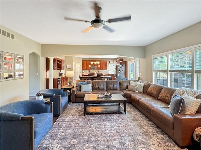 living area with arched walkways, visible vents, decorative columns, and ceiling fan