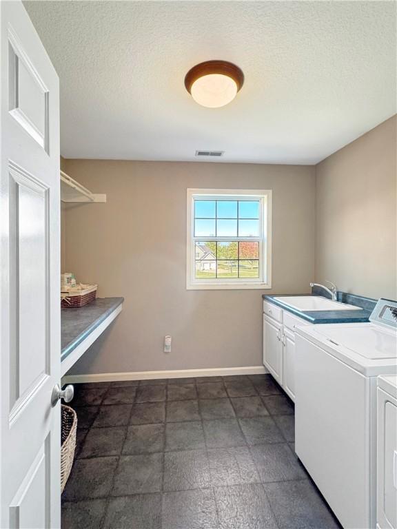 washroom featuring cabinet space, a sink, a textured ceiling, separate washer and dryer, and baseboards