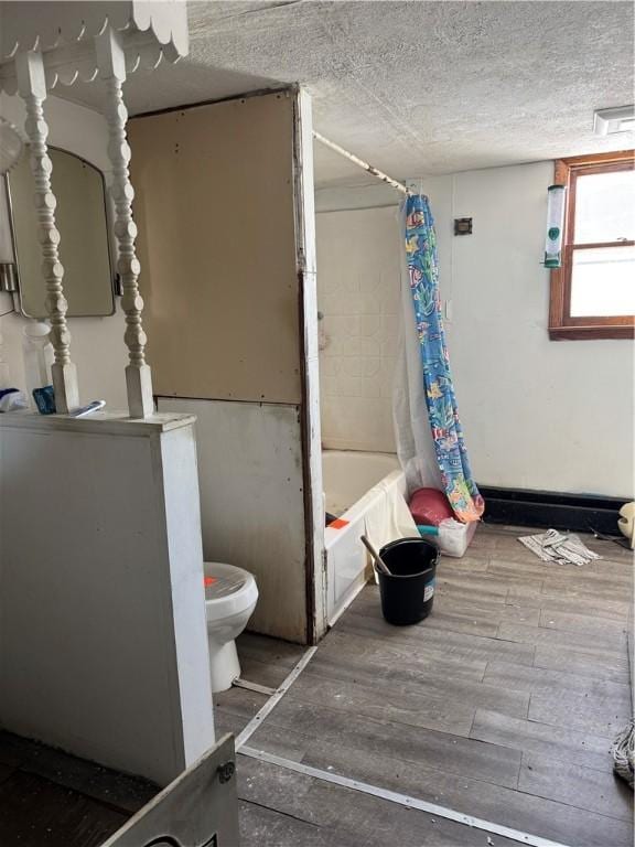 full bath featuring a textured ceiling, wood finished floors, toilet, and shower / bathtub combination with curtain