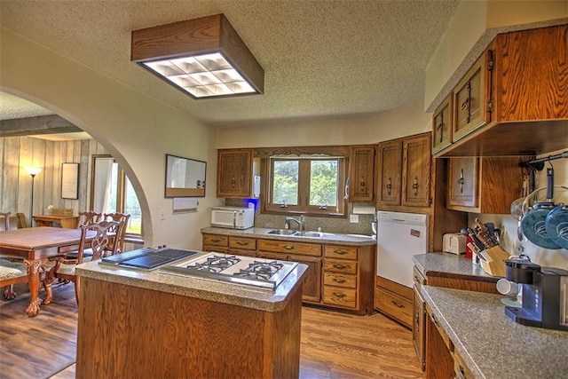 kitchen featuring brown cabinets, a sink, arched walkways, white appliances, and a textured ceiling