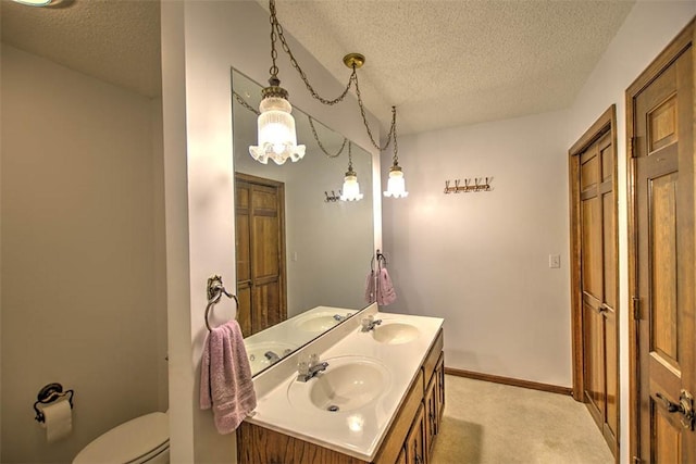 bathroom featuring toilet, a sink, a textured ceiling, and double vanity