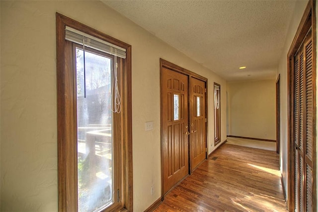 hall featuring baseboards, wood finished floors, and a textured ceiling