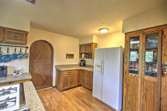 kitchen with brown cabinets, light wood-style floors, a textured ceiling, and white appliances