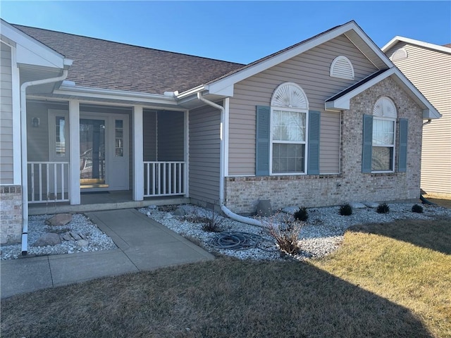 view of front facade with a porch, a shingled roof, brick siding, and a front yard