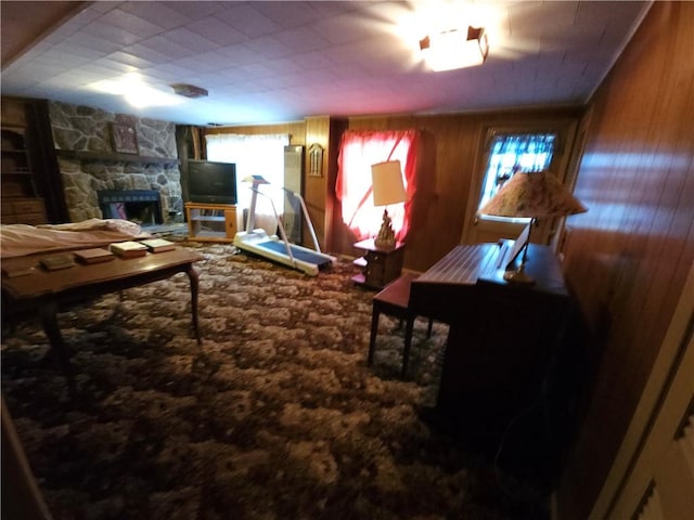 carpeted living area with a stone fireplace and wooden walls