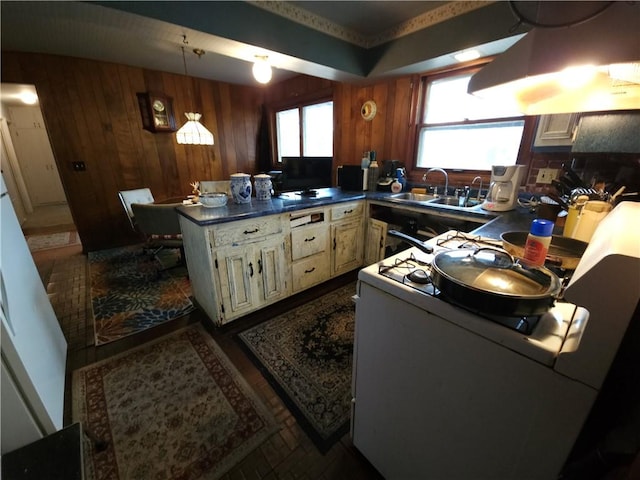 kitchen featuring white gas range, dark countertops, a sink, wooden walls, and ventilation hood