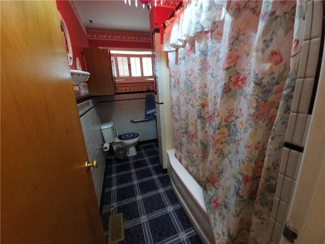 full bathroom with a wainscoted wall, shower / bath combo with shower curtain, toilet, and tile walls