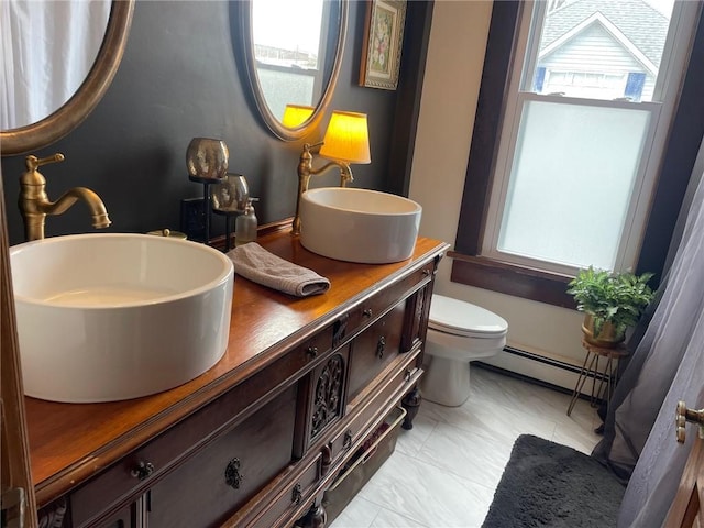 full bathroom featuring toilet, double vanity, a baseboard heating unit, and a sink