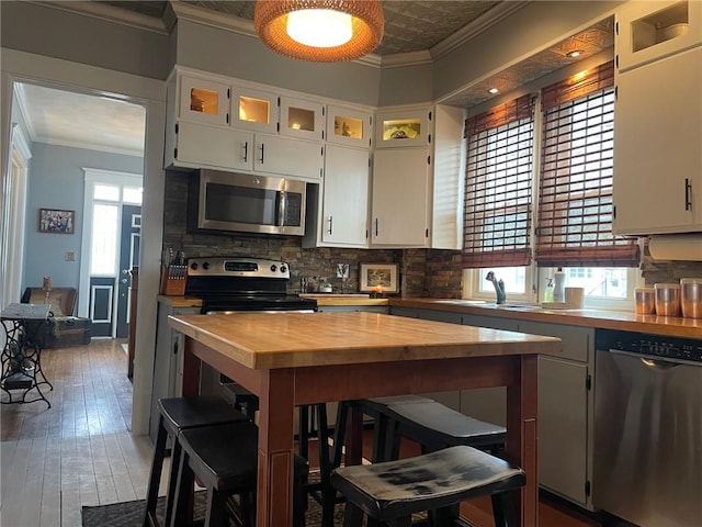 kitchen featuring a sink, ornamental molding, appliances with stainless steel finishes, wood counters, and backsplash