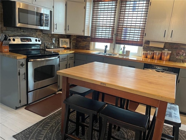 kitchen featuring gray cabinets, appliances with stainless steel finishes, decorative backsplash, and a sink