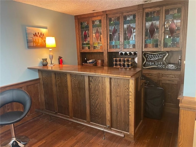 bar featuring wainscoting, hardwood / wood-style flooring, a textured ceiling, and a dry bar