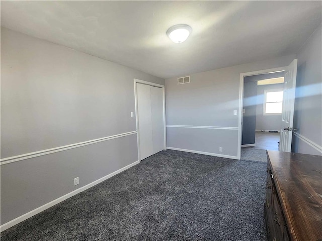 unfurnished bedroom featuring baseboards, visible vents, dark carpet, and a closet