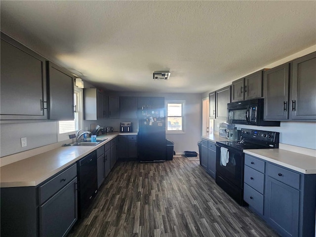 kitchen featuring dark wood-type flooring, light countertops, a healthy amount of sunlight, black appliances, and a sink