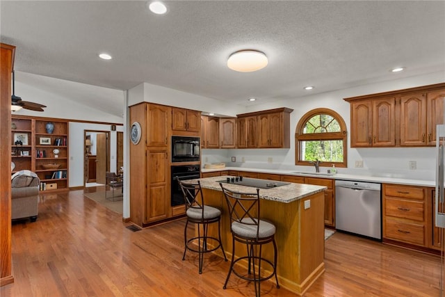 kitchen featuring a sink, a breakfast bar area, a center island, vaulted ceiling, and black appliances