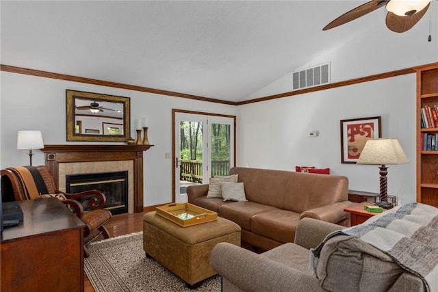 living area with ceiling fan, a fireplace, wood finished floors, vaulted ceiling, and visible vents