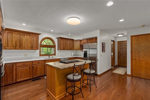 kitchen with a sink, stainless steel fridge with ice dispenser, brown cabinetry, a center island, and a kitchen bar