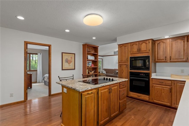 kitchen with brown cabinetry, a kitchen island, wood finished floors, and black appliances