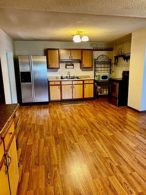 311 E Collett St, Oakwood, IL 61858 - kitchen featuring appliances with stainless steel finishes, wood finished floors, a textured ceiling, and brown cabinetry