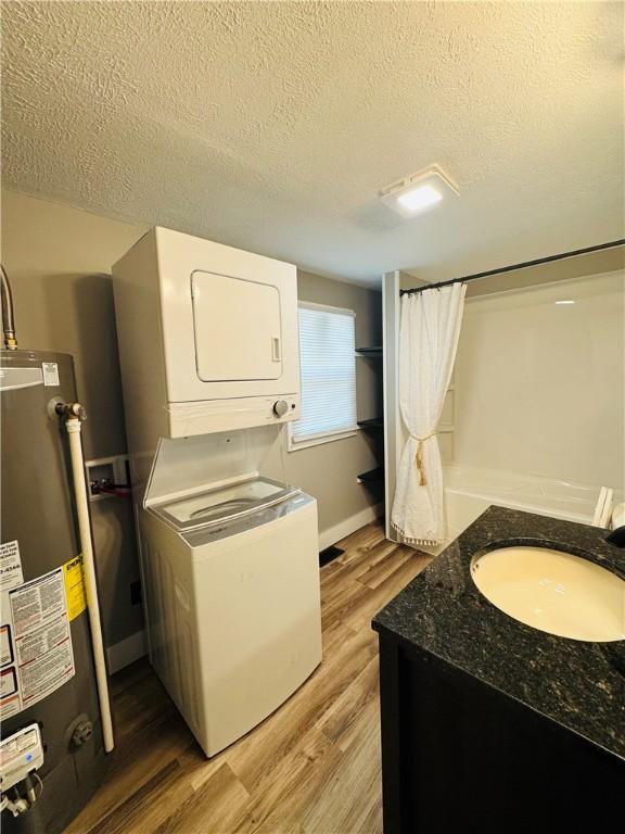 1404 N 24th St, Decatur, IL 62526 - laundry room featuring estacked washer and dryer, gas water heater, a textured ceiling, light wood-style flooring, and baseboards