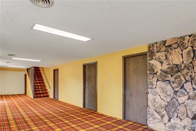 below grade area featuring stairway, a textured ceiling, visible vents, and carpet floors