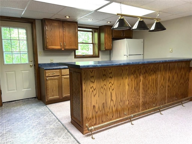 3002 N Charlotte St, Effingham, IL 62401 - kitchen featuring freestanding refrigerator, a paneled ceiling, dark countertops, brown cabinetry, and pendant lighting