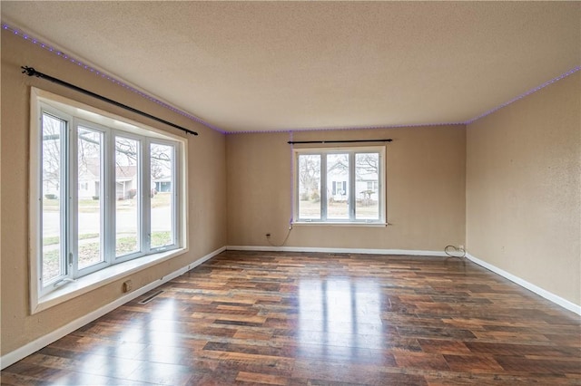 spare room with a textured ceiling, dark hardwood / wood-style floors, and a healthy amount of sunlight