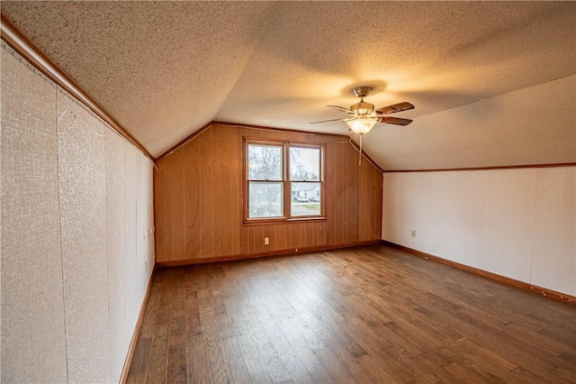 bonus room featuring wood walls, lofted ceiling, hardwood / wood-style flooring, ceiling fan, and a textured ceiling