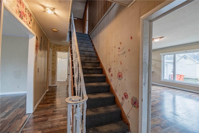 staircase with a textured ceiling, hardwood / wood-style flooring, and wood walls