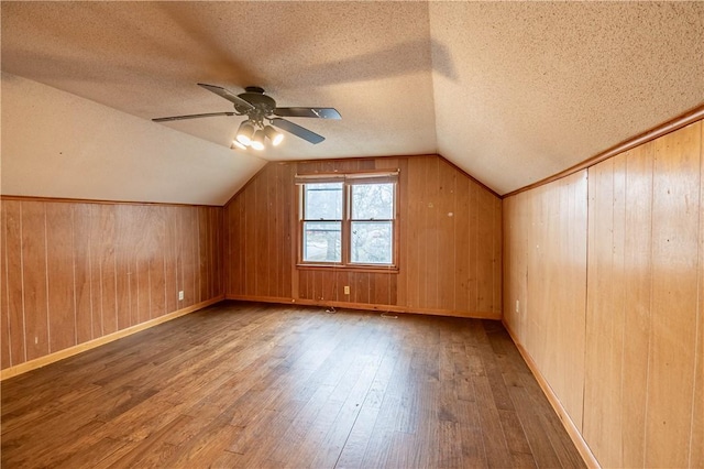 bonus room featuring wood-type flooring, a textured ceiling, vaulted ceiling, and wood walls