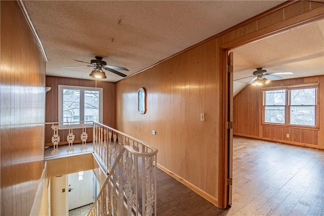 corridor featuring wood-type flooring, a textured ceiling, vaulted ceiling, and wood walls