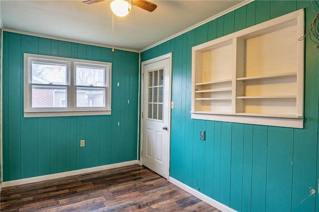 interior space with ceiling fan, wooden walls, dark wood-type flooring, and ornamental molding