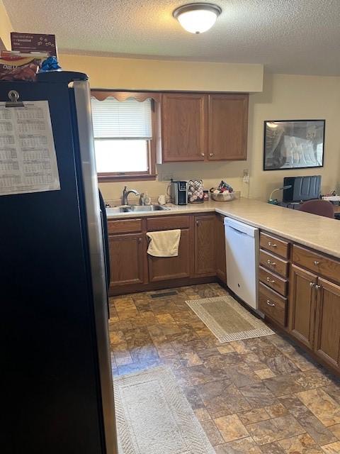 kitchen featuring freestanding refrigerator, a sink, white dishwasher, a textured ceiling, and light countertops