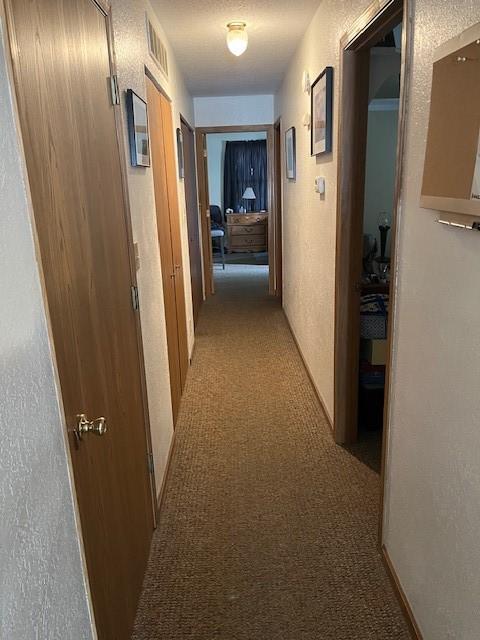 hall with light carpet and a textured wall