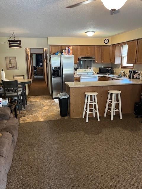 kitchen with stainless steel appliances, under cabinet range hood, light countertops, a peninsula, and a kitchen bar