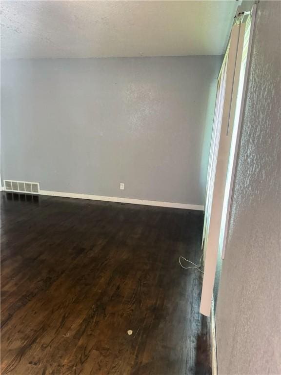 unfurnished room with visible vents, baseboards, and dark wood-style floors