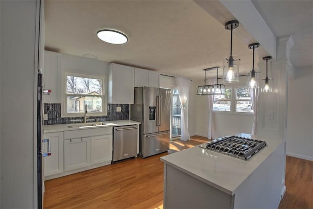 kitchen featuring appliances with stainless steel finishes, sink, white cabinets, decorative backsplash, and hanging light fixtures