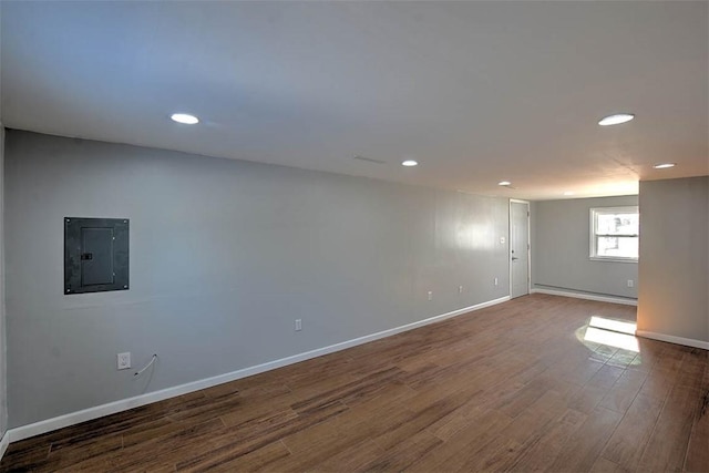 basement with a baseboard radiator, hardwood / wood-style floors, and electric panel